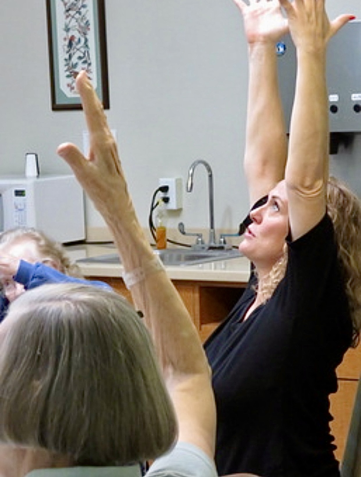 Close up of a woman guiding a seated stretch, arms raised