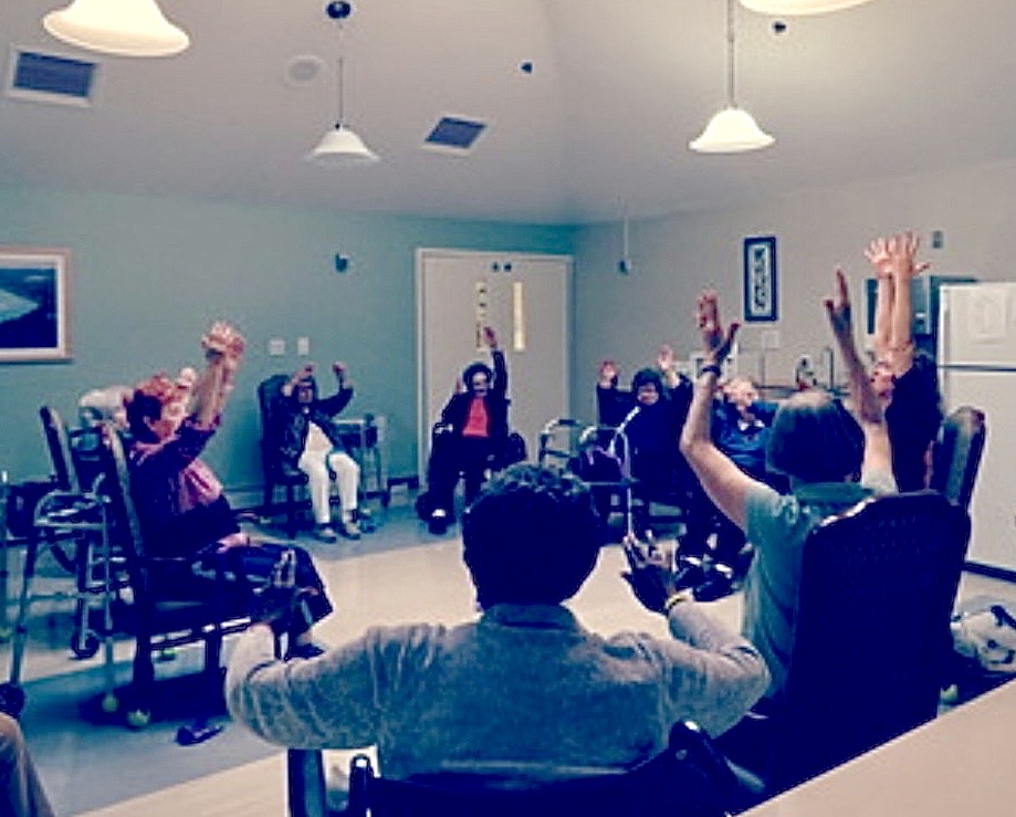 A seated chair yoga class, arms raised together